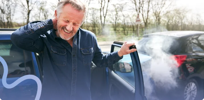 Man wincing and holding his neck while stepping out of his car after a collision