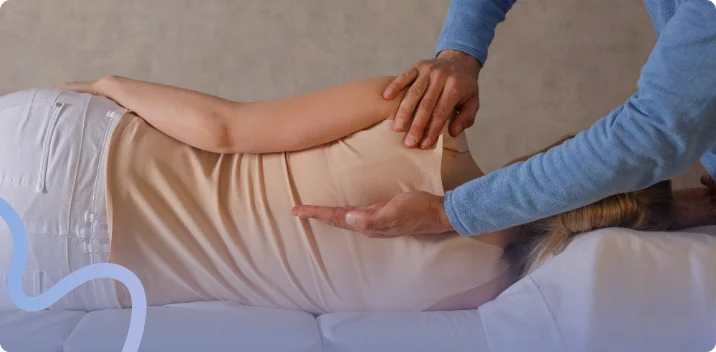 Chiropractor examining a patient's lower back as she lies on a treatment table