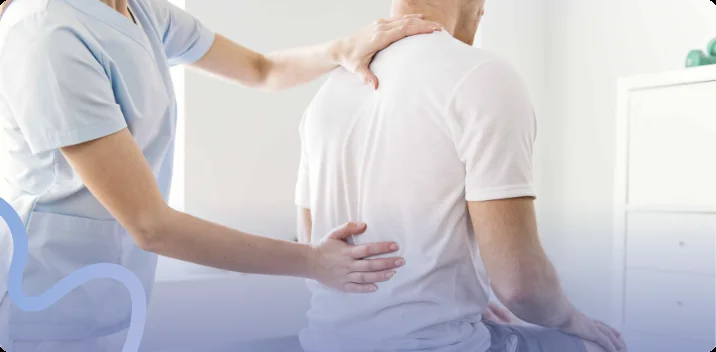 Chiropractor examining a seated patient's lower back and shoulder during an evaluation
