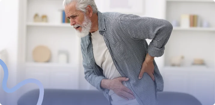 Older man grimacing and holding his hip while leaning forward at home