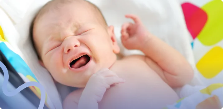 Crying newborn baby lying on a colorful blanket with a hand raised