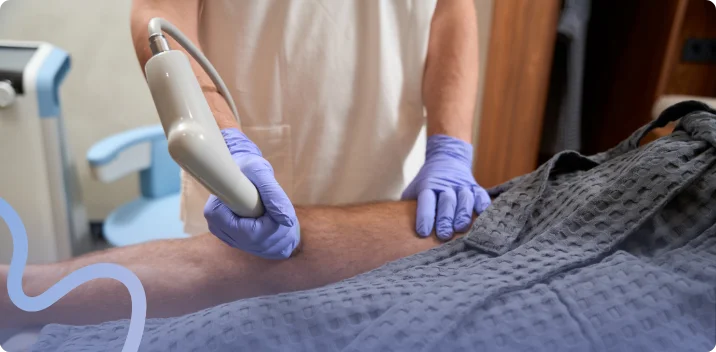 Gloved provider applying a therapy handpiece to a patient's knee during a treatment session