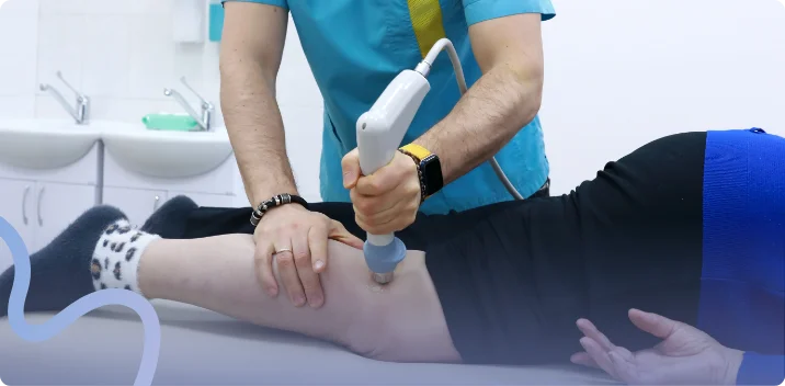 Provider applying a shockwave therapy handpiece to a patient's knee in a clinic