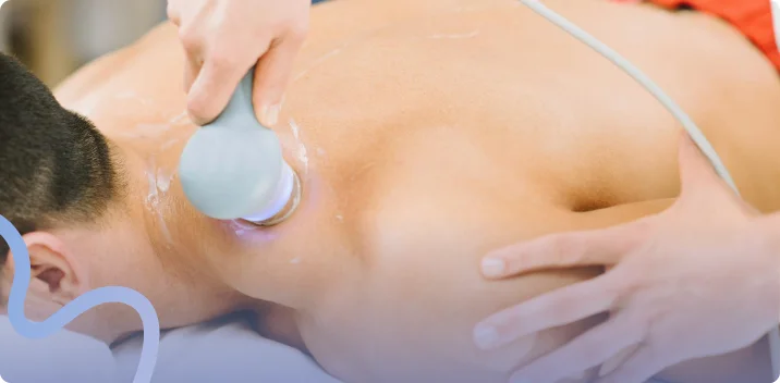 Provider applying a shockwave therapy handpiece to a patient's shoulder during a treatment visit