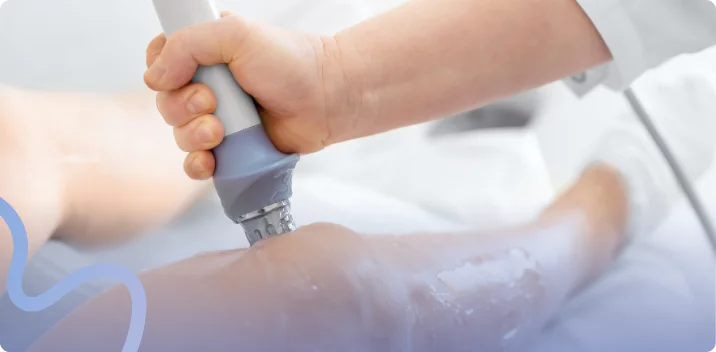 Clinician applying a shockwave therapy handpiece to a patient's knee during treatment