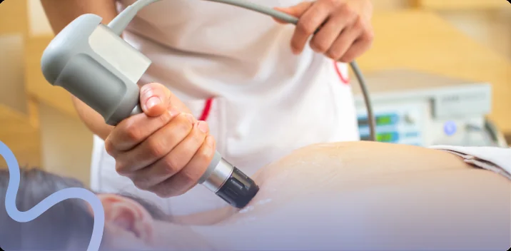 Clinician guiding a shockwave therapy applicator over a patient's shoulder with the control unit nearby