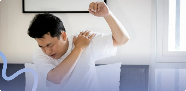 Man wincing and gripping his sore shoulder while raising his arm at home