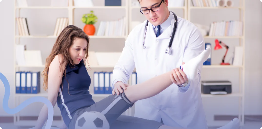 Sports medicine provider examining a young female athlete's injured leg with a soccer ball nearby