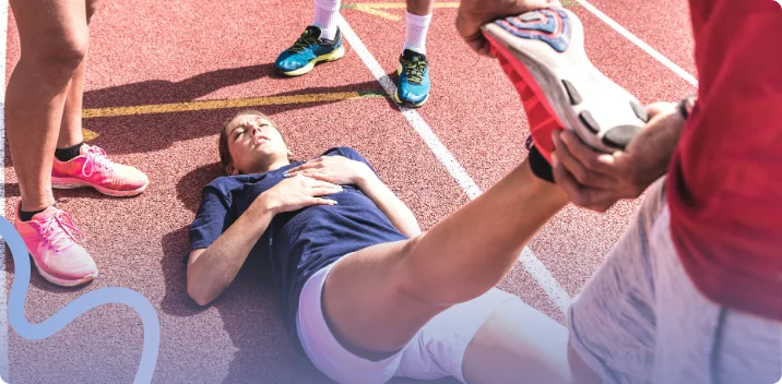 Athlete lying on a running track while a trainer examines her leg for a sports injury